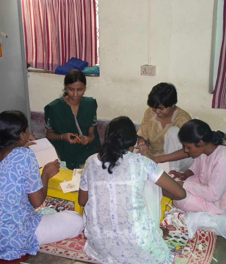 Sechs Frauen arbeiten gemeinsam an handwerklichen Tätigkeiten auf einem Teppichboden.